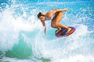 A young woman skimboarding on a wave off Sandy Beach, Oahu; Oahu, Hawaii, United States of America