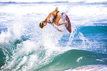 A young woman leaps in the air on a skimboard off Sandy Beach, Oahu; Oahu, Hawaii, United States of America