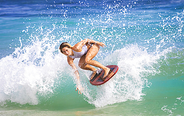 A young woman skimboarding on a wave off Sandy Beach, Oahu; Oahu, Hawaii, United States of America