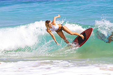 A young woman skimboarding on a wave off Sandy Beach, Oahu; Oahu, Hawaii, United States of America