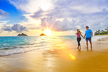 A couple walks on Lanakai beach on the Hawaiian island of Oahu at sunset; Lanakai, Oahu, Hawaii, United States of America