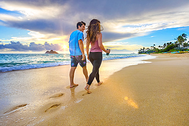 A couple walks on Lanakai beach on the Hawaiian island of Oahu at sunset; Lanakai, Oahu, Hawaii, United States of America