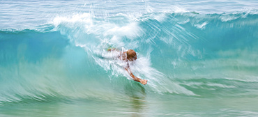 A man swims in the crest of a turquoise wave; Kihei, Maui, Hawaii, United States of America