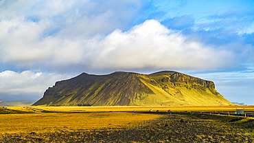 A rugged outcrop covered in green tundra with a road running through the vast landscape; Iceland