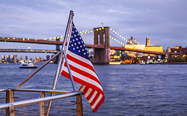 An American Flag flies from a railing at the waterfront with a view of the Brooklyn Bridge, Manhattan; New York City, New York, United States of America