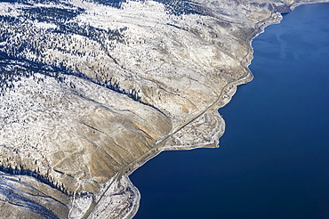 A remote coastline of blue ocean water and barren land with light snow cover along the coast of British Columbia; British Columbia, Canada