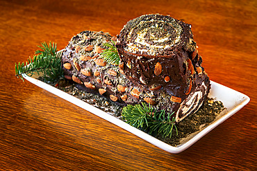 Close-up of decorative log cake with pine needle trimmings on a wooden table; Studio