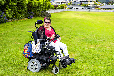 Maori woman with Cerebral Palsy in a wheelchair on a grass field in a park area; Wellington, New Zealand