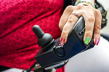 Maori woman with Cerebral Palsy in an electric wheelchair with a joystick and controllers, fingernails showing nail art; Wellington, New Zealand