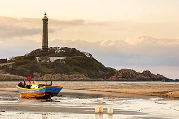 Colourful fishing boat tied to the beach and a lighthouse on a hill along the coast, Ke Ga Cape; Ke Ga, Vietnam