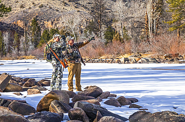 Hunters with camouflage clothing and rifle looking out with binoculars; Denver, Colorado, United States of America