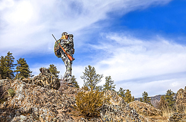 Hunter with camouflage clothing and rifle looking out with binoculars; Denver, Colorado, United States of America