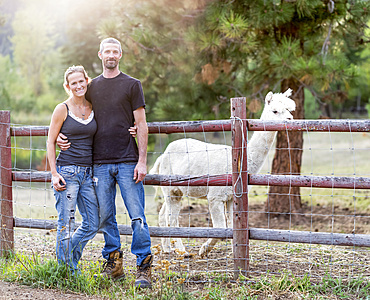 Portrait of a farmer and his wife with a llama (Lama glama) in the background; Armstrong, British Columbia, Canada