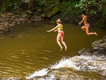 Two women wearing bikinis cliff jumping from the top of one of the Twin Falls waterfalls; Haiku, Maui, Hawaii, United States of America