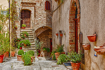 Exterior of an old, stone building with a staircase and three entrances to separate apartments with terracotta flower pots on the terrace as well as suspended on the stone walls; Volterra, Province of Pisa, Tuscany, Italy