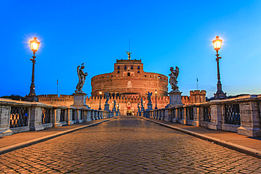 Ponte Sant'Angelo spanning the Tiber River and lined with statues of angels illuminated by lampposts at dusk and leading to the Castel Sant'Angelo (Mausoleum of Hadrian); Rome, Lazio, Italy