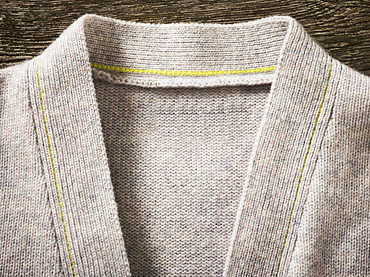 Collar and neckline of a grey cardigan sweater with yellow stitching; Studio