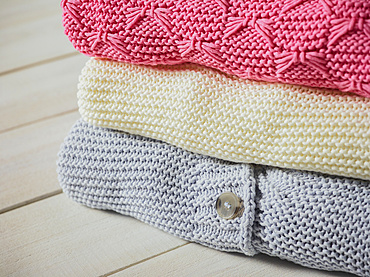 Three knit sweaters folded in a pile; Studio