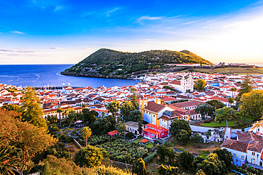 Scenic view overlooking Monte Brasil and the capital city of Angra do Heroismo,  with the sunset reflecting warm light on the whitewashed buildings and the brilliant blue Atlantic Ocean; Terceira, Azores