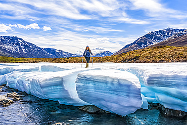 Woman hiking along the Dempster Highway enjoying the scenery, and standing on a piece of late season ice along the Klondike River in Tombstone Territorial Park; Yukon, Canada