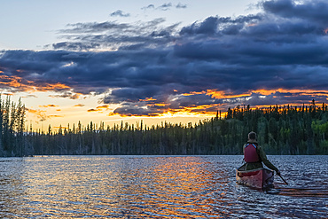 View taken from behind of person canoeing at sunset on a lake near Whitehorse; Yukon, Canada