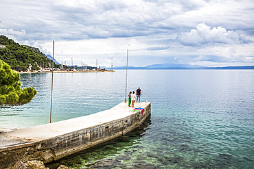 Tourists walk on a pier towards the turquoise water along the coast of Podgora, Croatia. This group has stopped for an early morning swim and shower after camping in their van; Podgora, Split-Dalmatia County, Croatia