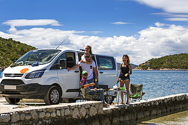 A group of friends standing and eating in the sun outside their camper van as they make a stop in Slano for an afternoon at the beach; Slano, Dubrovacko-neretvanska zupanija, Croatia