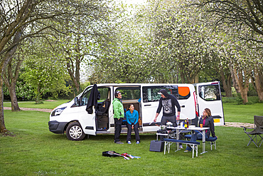 Friends setting up camp outside of a modified caravan camper; Bourton-on-the-Water, England, United Kingdom