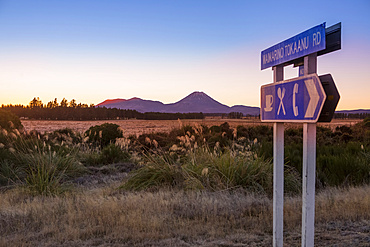 A beautiful sunset in the Tongariro National Park. The volcanic Mount Doom (Mount Ngauruhoe) can be seen in the background, with a roadside sign in the foreground; Manawatu-Wanganui, New Zealand