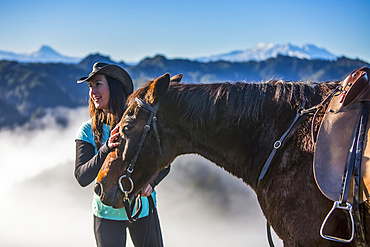 The Blue Duck lodge located in the Whanganui National Park is a working cattle farm with a focus on conservation. Travellers go to a scenic viewpoint to watch the sunrise over the rainforest. A Cowgirl stands with her horse; Retaruke, Manawatu-Wanganui, New Zealand