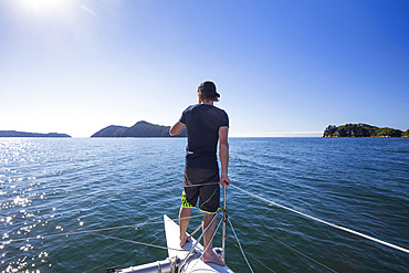 View taken from behind of a man standing at the bow of a catamaran on a boat tour in the Abel Tasman National Park; Tasman, New Zealand