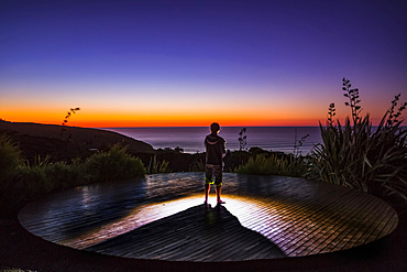 A man watches the sunset from the cliffs of Raglan, New Zealand; Raglan, Waikato, New Zealand