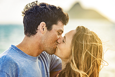 Millennial couple kissing on Lanikai Beach with the Mokes Islands in the background; Lanikai, Oahu, Hawaii, USA