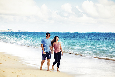 A Millennial couple walking along Lanikai Beach with Mokapu Point and the Moku Manu Islands in the background; Lanikai, Oahu, Hawaii, USA