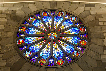 A colourful stained glass window in a circle-shape with intricate designs and symbols on a stone wall; Nelson, Nelson Province, New Zealand