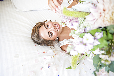 A bride laying on bed in her bridal suite whilst holding a bouquet of flowers