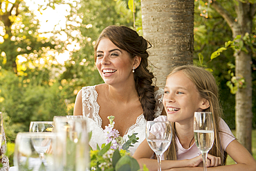 A bride sits with a young girl at the top table at an outside wedding