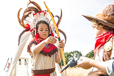 A young brother and sister play cowboys and indians outside