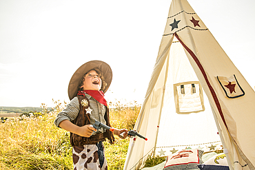 A young boy plays cowboys and indians outside in the sunshine