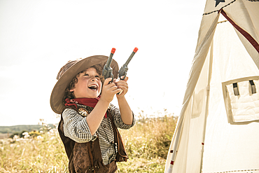 A young boy plays cowboys and indians outside in the sunshine