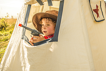 A young boy plays cowboys and indians outside in the sunshine