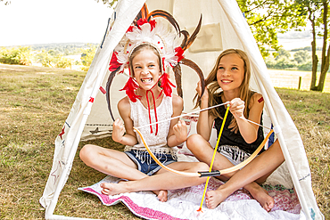 Young twins sit in a wigwam outside in the sunshine