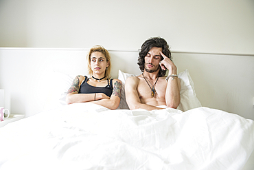 A cool young tattooed couple lying in a double bed after an arguement.