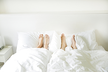 A couple lying in a bed with their feet sticking out from underneath the covers.