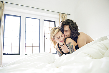 A cool young tattooed couple cuddling on a bed.