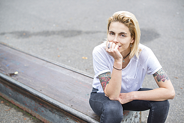 A cool young tattooed blond girl sitting in a skatepark.