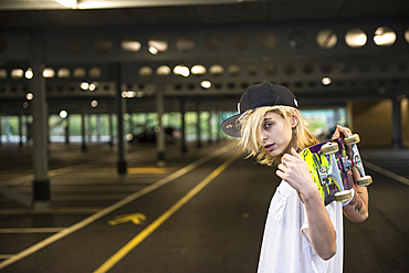 A cool young tattooed skater girl carrying her skateboard over her shoulders.