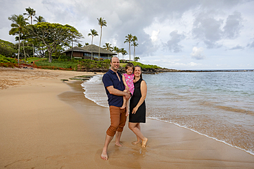 Portrait of a family standing on the shore and smiling at the camera along the sandy beach at Kapalua Resort in West Maui, Maui, Hawaii, United States of America