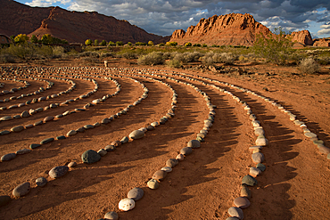 Hiking trail through Snow Canyon, with circles of stones in a meeting area behind the Red Mountain Spa, with meditation maze and Snow Canyon Mountain Range in the background. Red Cliffs Desert Reserve around St George Town with rock cliffs and dark clouds in a blue sky, St George, Utah, United States of America