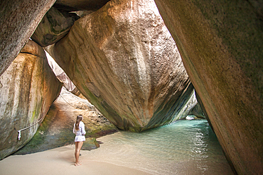 Woman standing under the large, boulders on the seaside shores of The Baths, a famous beach in the BVI's, Virgin Gorda, British Virgin Islands, Caribbean